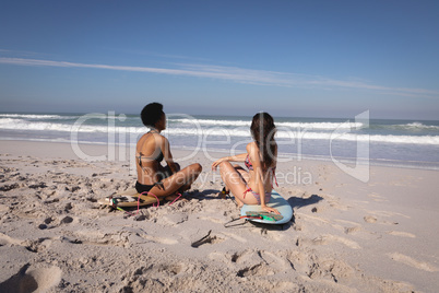 Young women sitting on surfboard at beach in the sunshine