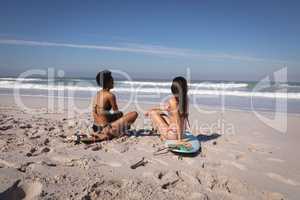 Young women sitting on surfboard at beach in the sunshine