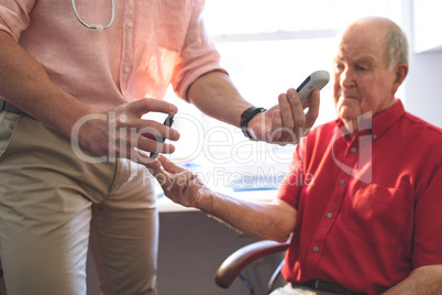 Confident male doctor examining senior man patient with glucometer