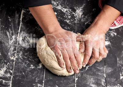 baker kneads white wheat flour dough on a black wooden table