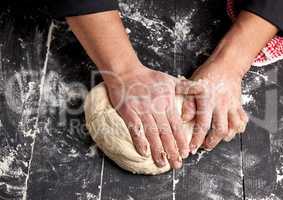 baker kneads white wheat flour dough on a black wooden table