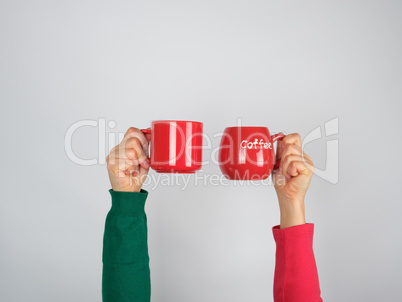 two hands in a sweater holding red ceramic mugs
