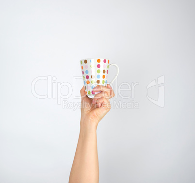 ceramic cup with multi-colored circles in a female hand on a whi