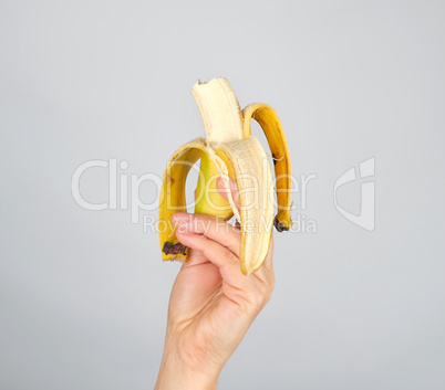 peeled fresh banana in a female hand on a white background
