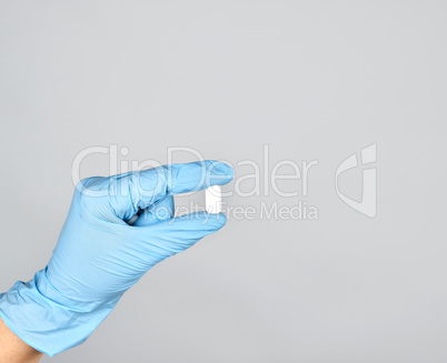 blue sterile gloved hand holding a white pill