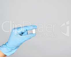 blue sterile gloved hand holding a white pill