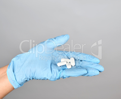 blue sterile gloved hand holding white pills