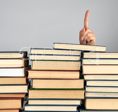 stack of different books on a gray background, hand sticks out f