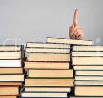 stack of different books on a gray background, hand sticks out f