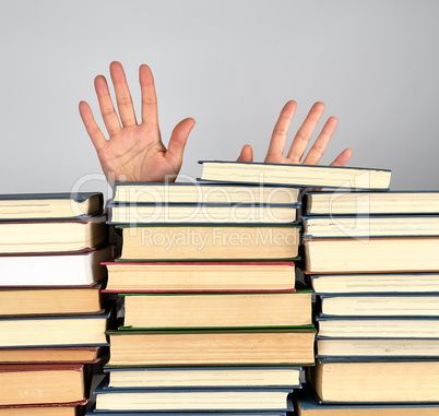 a stack of different books on a gray background, two female hand