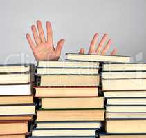 a stack of different books on a gray background, two female hand