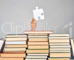 female hand holding a big white puzzle and a stack of books