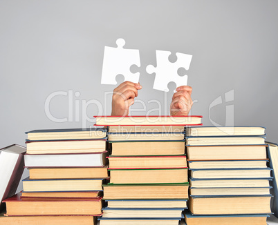 female hands holding big white puzzles over a stack of books