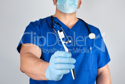 Doctor in sterile latex gloves and blue uniform holding a toothb