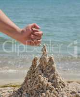 hand builds a castle from the wet sea sand on the beach
