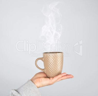 female hand holding a brown ceramic mug with a drink