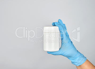 hand in blue sterile glove holds white plastic jar with pills