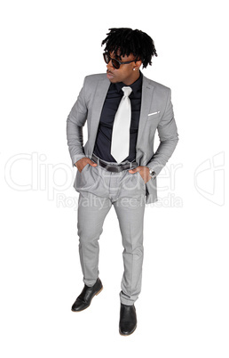 A black young man standing in a gray suit and sunglasses