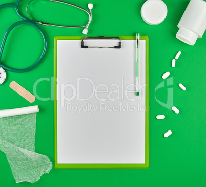paper holder with empty white sheets, medical stethoscope, pills