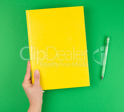 female hand holding a yellow closed notebook and pen