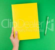 female hand holding a yellow closed notebook and pen