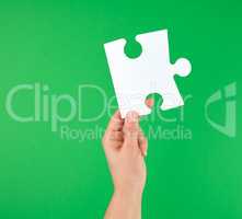white big puzzle in female hand on green background