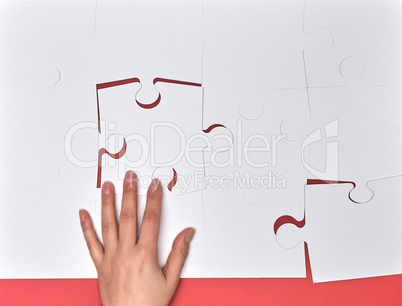 female hand puts white big puzzles on a pink background