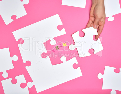 female hand puts white big puzzles on a pink background