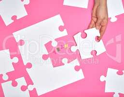 female hand puts white big puzzles on a pink background