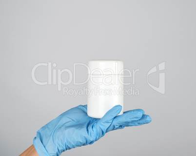 hand in blue sterile glove holds white plastic jar with pills