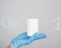 hand in blue sterile glove holds white plastic jar with pills