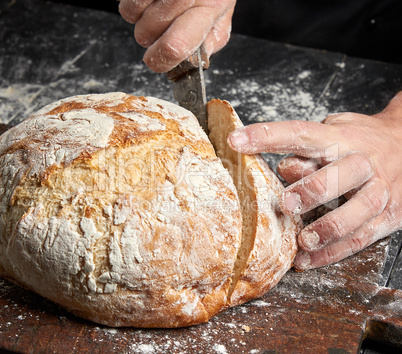 male hands cut a knife round baked bread male hands cut a knife round baked bread