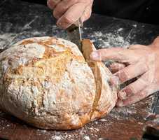 male hands cut a knife round baked bread