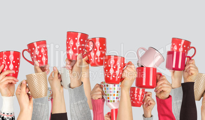 many raised hands up with ceramic cups on a white background