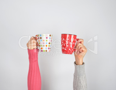 two hands in a sweater holding  ceramic mugs
