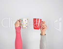 two hands in a sweater holding  ceramic mugs