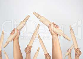 many hands raised up and holding kitchen wooden rolling pins