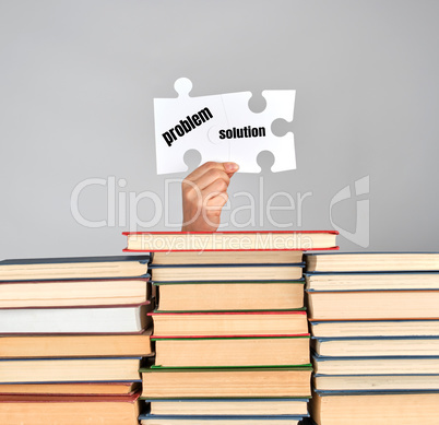 female hands holding big white puzzles over a stack of books