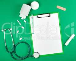 paper holder with empty white sheets, medical stethoscope, pills