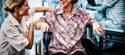 Cheerful disabled senior woman sitting on wheelchair looking at female doctor