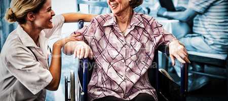 Cheerful disabled senior woman sitting on wheelchair looking at female doctor