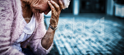 Side view of depressed senior woman sitting on bench with head in hand