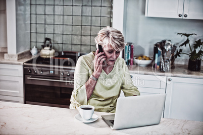 Senior woman talking on mobile phone while using laptop