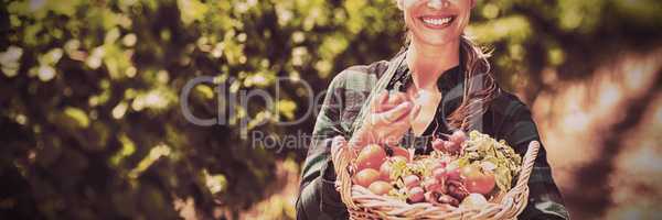 Portrait of happy female farmer holding a basket of vegetables