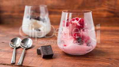 Pink and white ice cream in glass on wooden table.