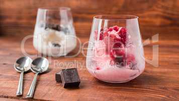 Pink and white ice cream in glass on wooden table.