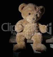 aold brown teddy bear is sitting on a wooden surface