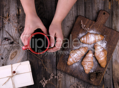 female hands holding a red ceramic cup with black coffee, next t