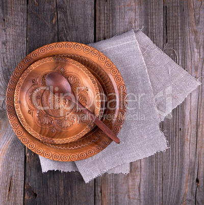 empty round brown carved decorative plate stands on a gray linen