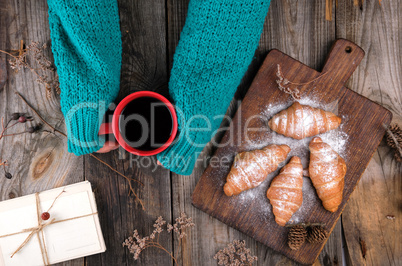 women's hands in a green knitted sweater holding a red ceramic m